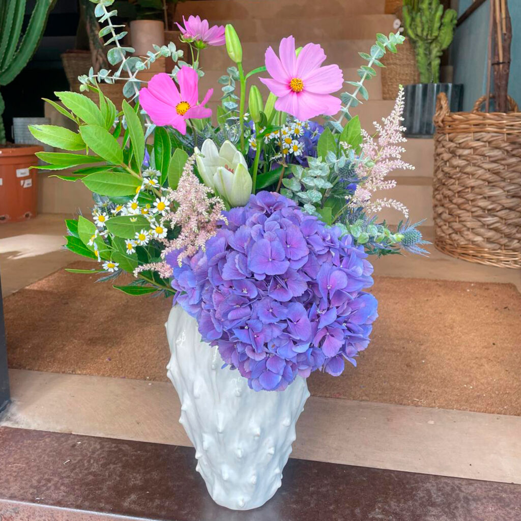 ramo de flores frescas en tonos violetas y rosas en jarrón blanco de cerámica