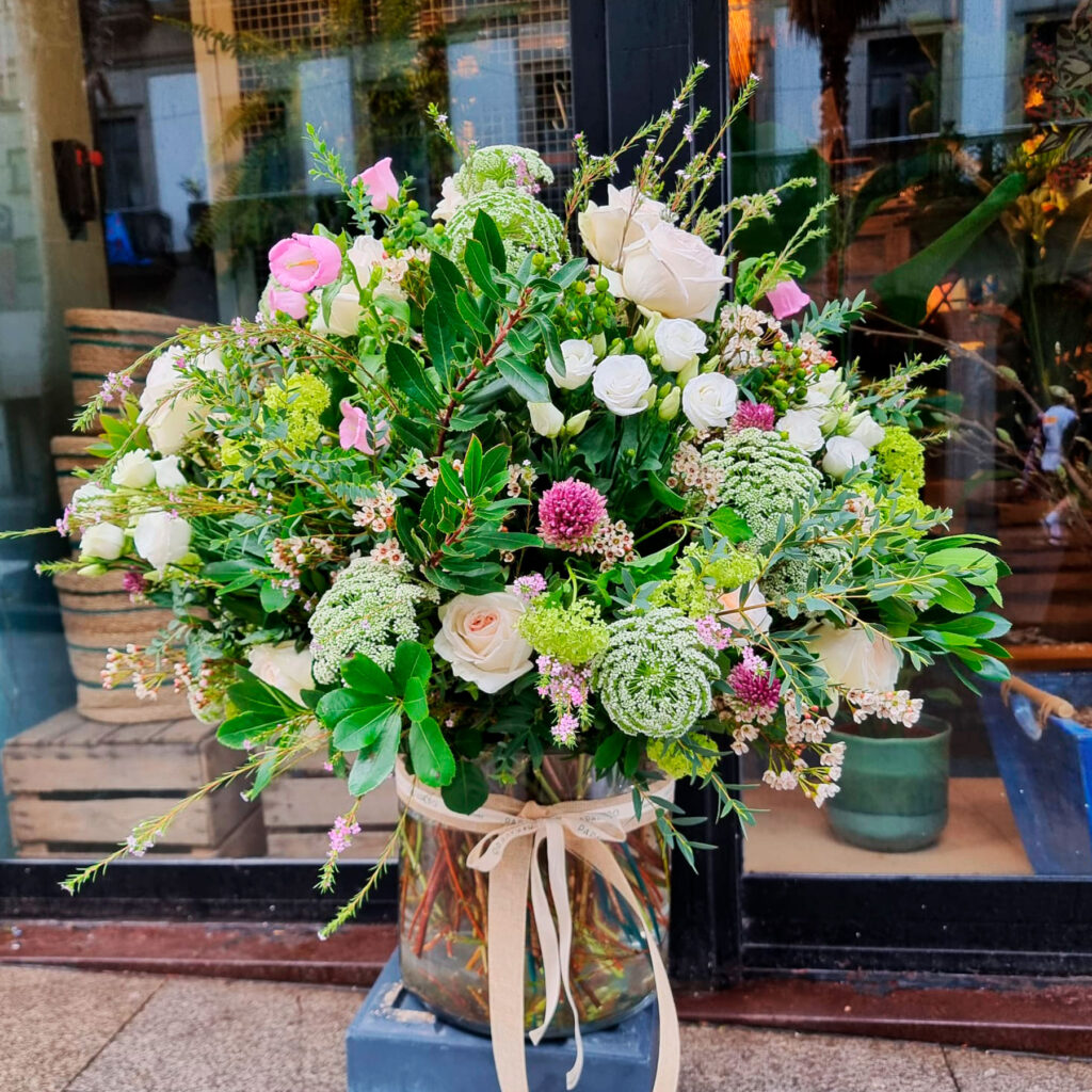 ramo de flores frescas en tonos rosas y blancos con verde decorativo en jarrón de cristal